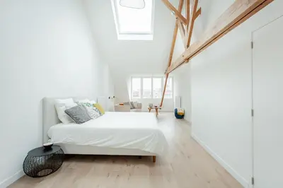 a white bedroom with a bed and wooden floors at RODELIJV in Ghent