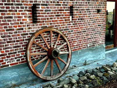 a wooden wagon wheel on the side of a brick wall at Burgemeestershof in Wetteren