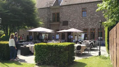 a group of people standing outside of a building with tables and umbrellas at Hotel ABBEY in Grimbergen