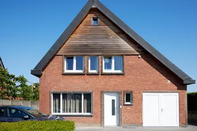 a red brick house with two white garage doors at Apartment with a view and parking in Brecht