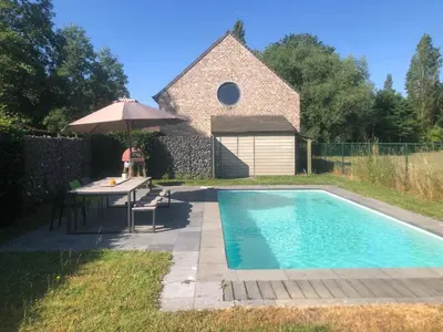 a swimming pool with a table and an umbrella at landelijke villa met zwembad en gezellige openhaard in Zemst