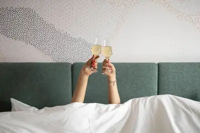 a woman laying in bed holding wine glasses at voco Brussels City North by IHG in Vilvoorde