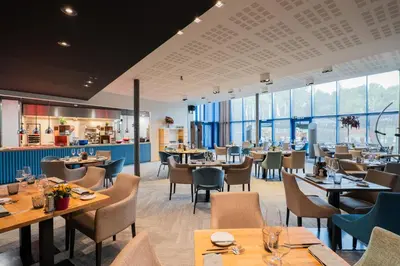a restaurant with wooden tables and chairs and windows at voco Brussels City North by IHG in Vilvoorde