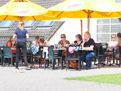 a group of people sitting at tables under an umbrella at Vakantiepark Breebos: Empty Lots for tents and mobile homes in Rijkevorsel