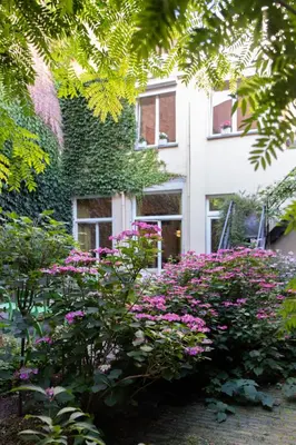 a garden with pink flowers in front of a building at Pauline Loveling apartment with quiet garden and 2 bathrooms in Antwerp