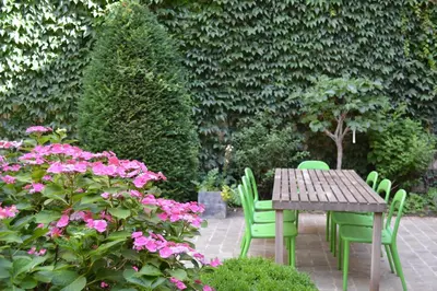 a wooden table and chairs in a garden with pink flowers at Pauline Loveling apartment with quiet garden and 2 bathrooms in Antwerp