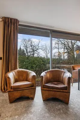 two leather chairs sitting in front of a window at Stylish lakehouse in idyllic, private green scenery in Stekene
