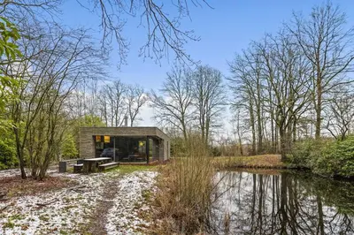 a cabin in the woods next to a body of water at Stylish lakehouse in idyllic, private green scenery in Stekene