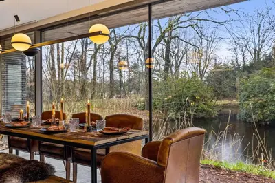a dining room with a table and a view of a river at Stylish lakehouse in idyllic, private green scenery in Stekene