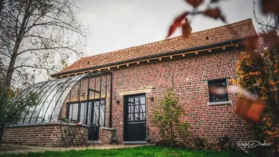 a brick house with a glass greenhouse behind it at Het Ovenhuisje in Denderwindeke
