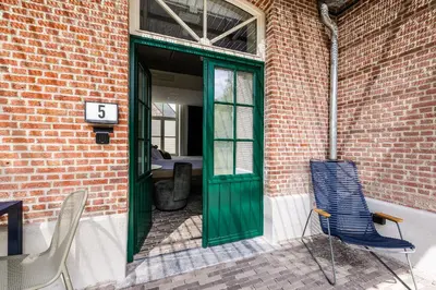a green door on a brick building with two chairs at Gare 55 in Evergem
