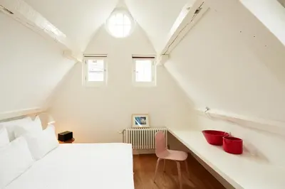 a attic bedroom with a bed and a pink chair at Hotel des Galeries in Brussels