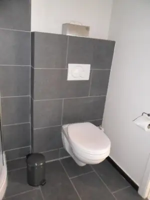 a bathroom with a toilet and a gray tiled wall at B&B Caramel in Turnhout