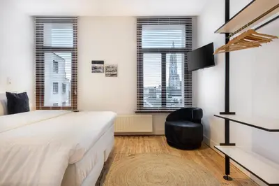 a bedroom with a bed and a chair and windows at The 1894 Boutique Holiday Apartment in Antwerp