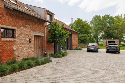 a brick building with two cars parked on a driveway at The barn - Waasmunster in Waasmunster