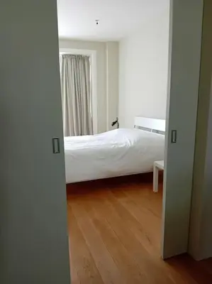 a bedroom with a white bed and a wooden floor at Spacieux Appartement 1 chambre double & jardin in Brussels