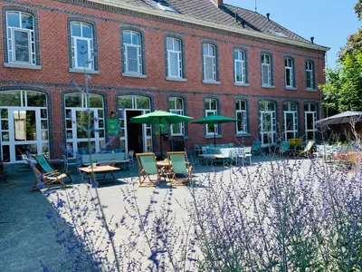 a building with chairs and umbrellas in front of it at De Lotuspoort met Mihr's B&B in de Abdij van Bornem in Bornem