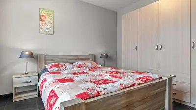 a bedroom with a bed with a red and white comforter at An's Vakantiehuisje in Dessel
