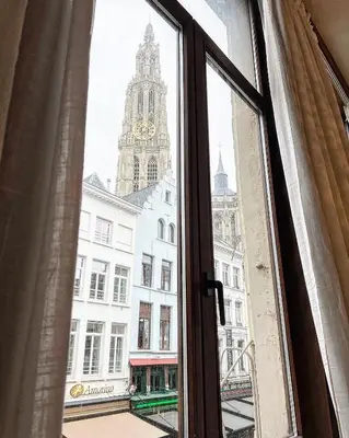 a window with a view of a building with a clock tower at LouLou Home's in Antwerp