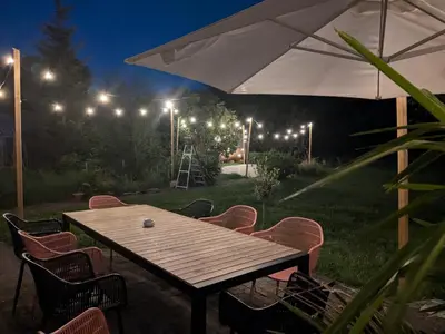a wooden table with chairs and an umbrella at night at BNB Green refuge: Vakantiehuis met zeer grote tuin in Londerzeel