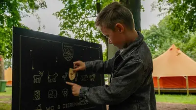 a young boy writing on a sign in a park at KARIBU - Olifant in Kasterlee