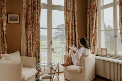 a woman sitting in a chair reading a book in a window at B&B Kasteel Den Tip in Arendonk