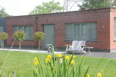 a red brick building with a chair and a table at B&B Het KoeKoeKsnest Schelle in Schelle