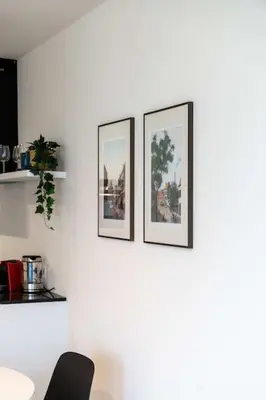 three framed pictures on a white wall with a chair at Beautiful 1BR apartment in Antwerp in Antwerp