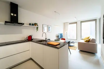 a white kitchen with a sink and a living room at Beautiful 1BR apartment in Antwerp in Antwerp