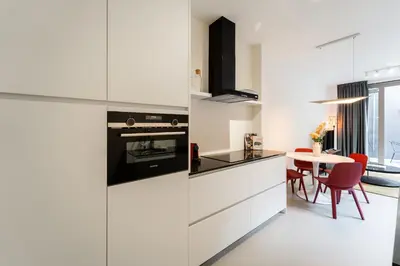 a kitchen with white cabinets and a table with red chairs at Apartments in Antwerp South in Antwerp