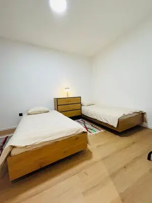 two beds in a white room with wooden floors at Cozy Flat in Brussels