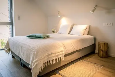 a bedroom with a large bed with white sheets at Vakantiewoning De Woestijn - De Schuur in Roosdaal