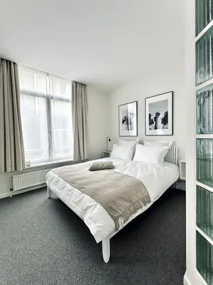 a white bedroom with a large bed and two windows at Magnifique appartement au coeur du SABLON ! in Brussels
