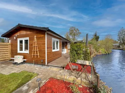a wooden house with a deck next to a river at Fonnies Chalet in Geel