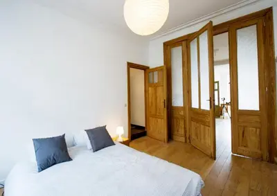 a bedroom with a white bed and wooden doors at Grand appartement d'artiste cosy et proche de tout in Brussels