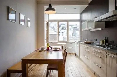 a kitchen with a wooden table and a large window at Grand appartement d'artiste cosy et proche de tout in Brussels