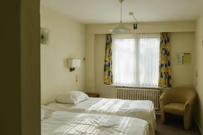a bedroom with a bed and a chair and a window at Hotel Kempenrust in Kasterlee