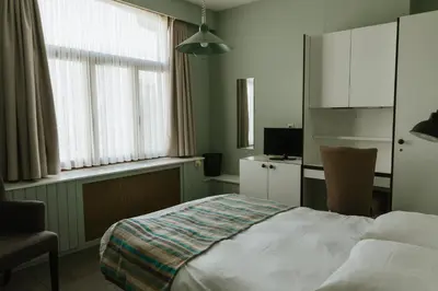 a bedroom with a bed and a chair and window at Hotel Kempenrust in Kasterlee