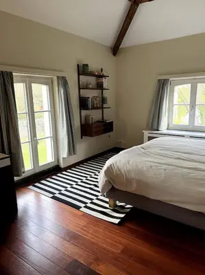 a bedroom with a bed and two windows and a rug at Charmante maison dans un coin de verdure à Boitsfort in Brussels