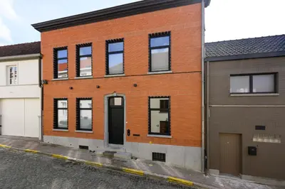 an orange brick building with a black door on a street at Huis Velzeke in Zottegem