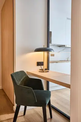 a green chair sitting next to a desk with a lamp at Georges Henri Aparthotel in Brussels