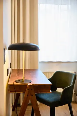 a desk with a lamp and a chair next to a window at Georges Henri Aparthotel in Brussels