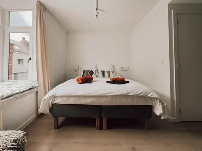 a white bedroom with a large bed with orange pillows at Business Accommodation 'Flow Living' Nomad in Geel