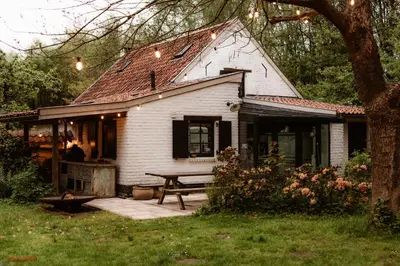 a white house with a picnic table in front of it at La Petite Foret Cottage in Brussels Countryside in Asse