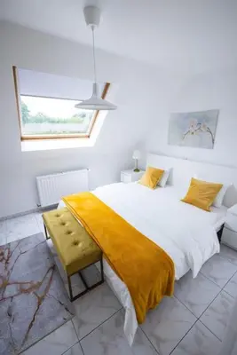 a white bedroom with a large bed with a yellow blanket at Résidence Orchidée in Zaventem