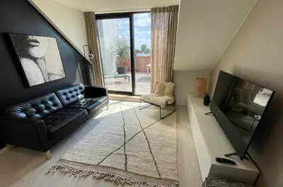 a living room with a black leather couch and a television at Penthouse with Airconditioning and Big Terrace, Close to Gent Sint-Pieters Station and City Centre in Ghent