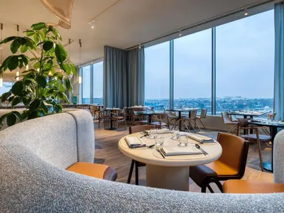 a restaurant with tables and chairs and large windows at Mövenpick Hotel Brussels Airport in Zaventem