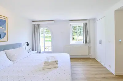 a white bedroom with a white bed and two windows at Le cottage de la Verte Voie in Wavre