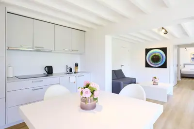 a white kitchen and living room with a table and chairs at Le cottage de la Verte Voie in Wavre