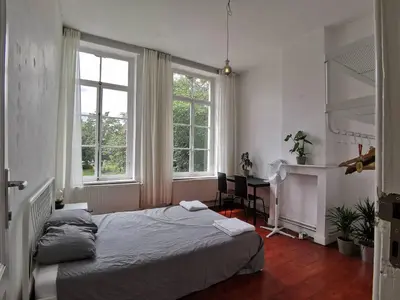 a bedroom with a bed and a desk and two windows at Cozy city centre room with parkview in Ghent